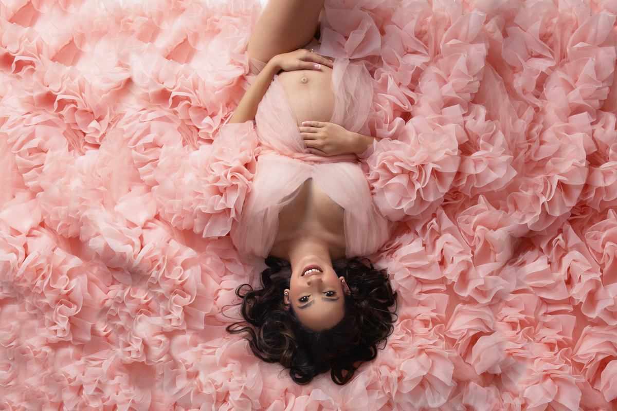 Pregnant woman lying down on a bed of pink tulle