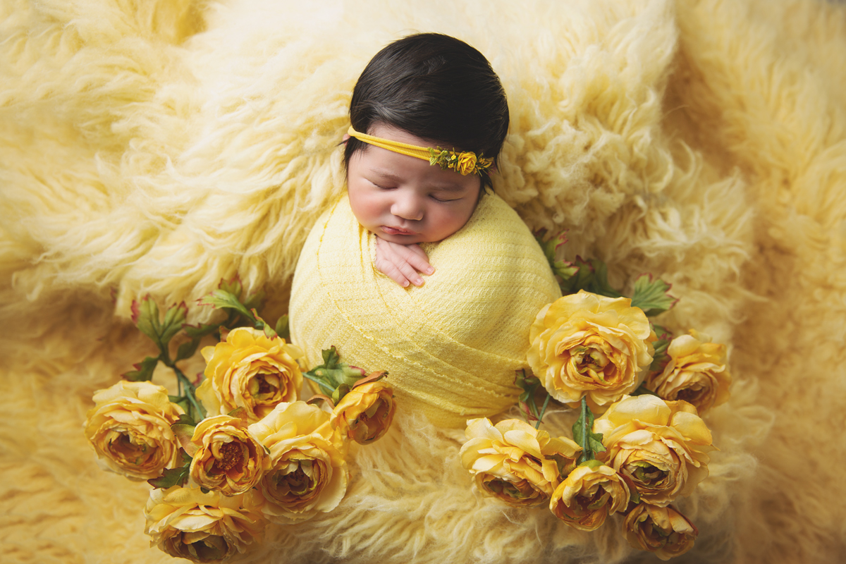 Newborn on yellow rug with yellow flowers