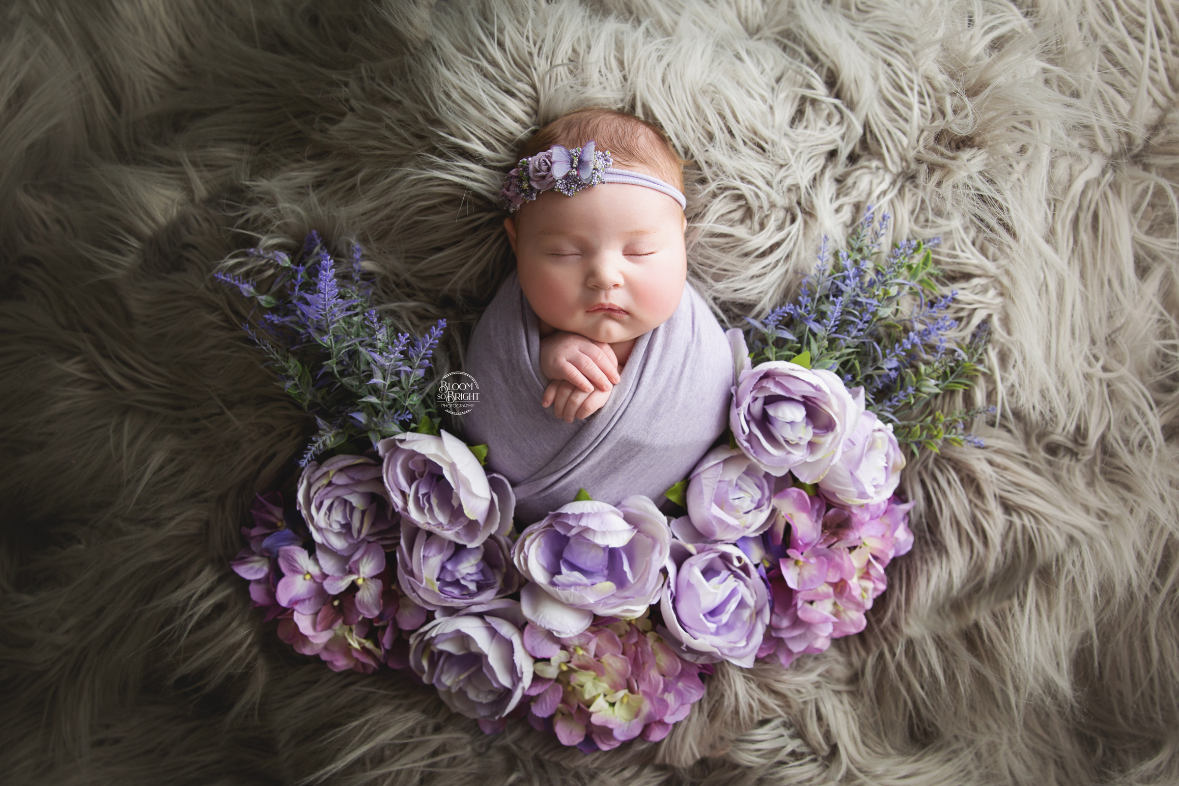Newborn on gray flokati with lavender and pink flowers